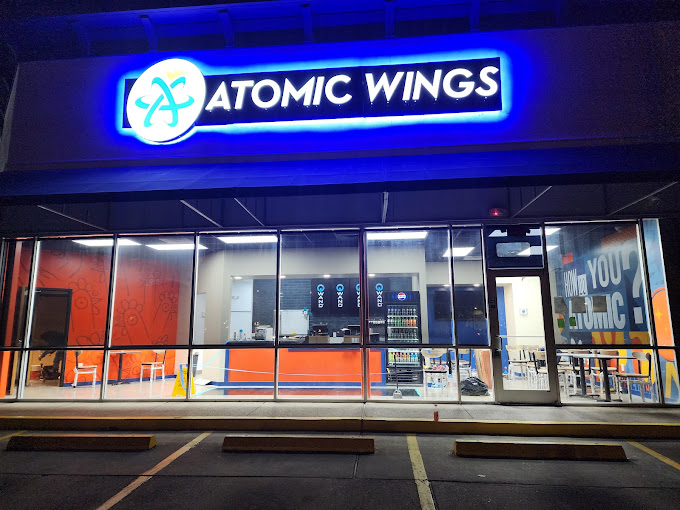 Front exterior view of Atomic Wings Houston restaurant at night, showcasing bright neon signage and modern glass storefront.